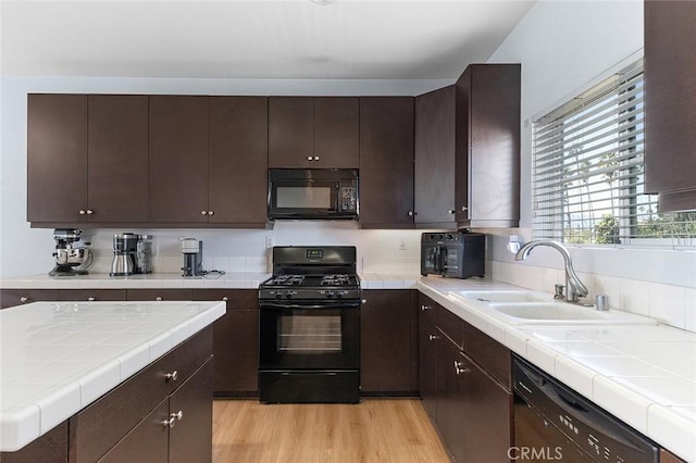 kitchen with light wood-type flooring, black appliances, a sink, dark brown cabinetry, and tile counters