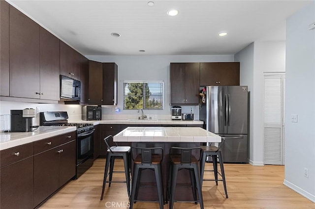 kitchen featuring a kitchen bar, black appliances, tile counters, and dark brown cabinetry