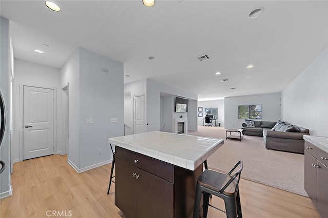 kitchen with a glass covered fireplace, light wood-style flooring, a breakfast bar area, and tile counters