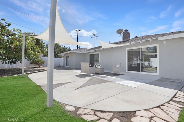 rear view of house featuring fence, a yard, a chimney, stucco siding, and a patio area