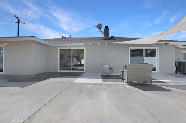 rear view of house featuring a patio area, central air condition unit, stucco siding, and a shingled roof