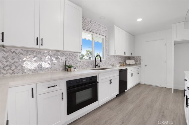 kitchen with a sink, black appliances, light countertops, light wood-style floors, and white cabinetry