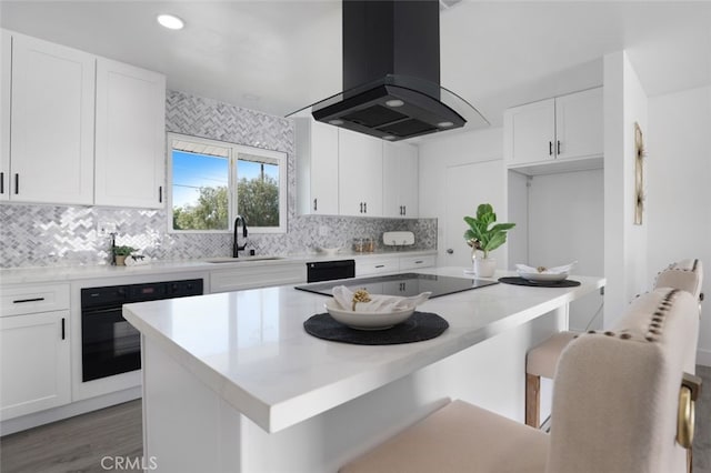 kitchen with a breakfast bar, island exhaust hood, white cabinets, black appliances, and a sink