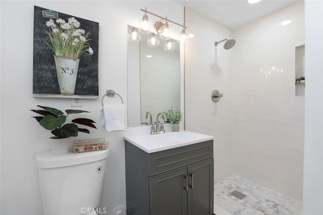 full bathroom with a tile shower, toilet, and vanity