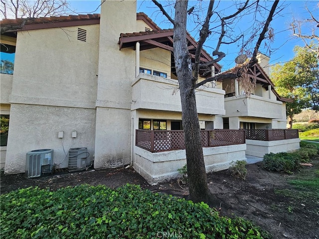 view of side of property with stucco siding, a tiled roof, and central AC