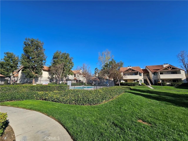 view of property's community featuring a residential view, a lawn, and fence