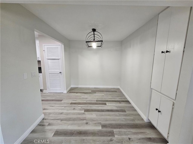 unfurnished dining area featuring an inviting chandelier, baseboards, and light wood finished floors