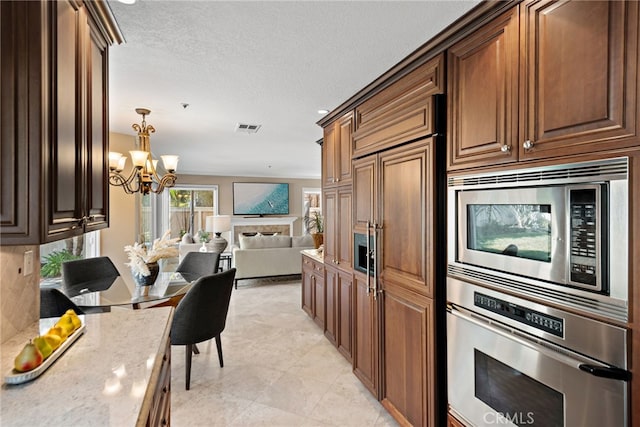 kitchen featuring light stone countertops, visible vents, built in appliances, open floor plan, and a chandelier