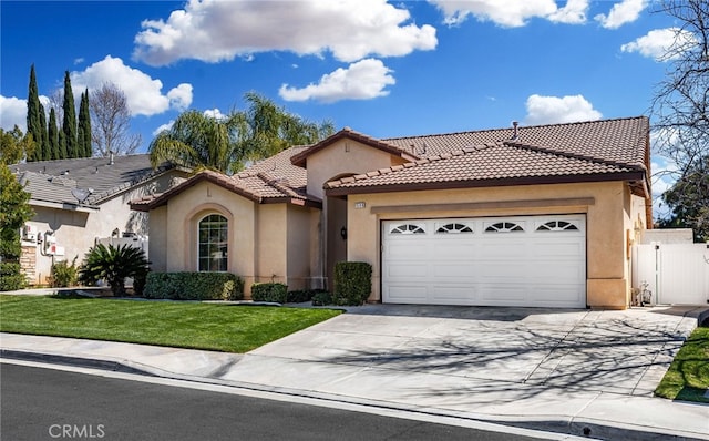 mediterranean / spanish-style home featuring a tile roof, a front yard, stucco siding, a garage, and driveway