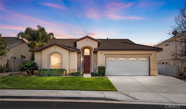 mediterranean / spanish house with a tile roof, concrete driveway, stucco siding, a yard, and an attached garage