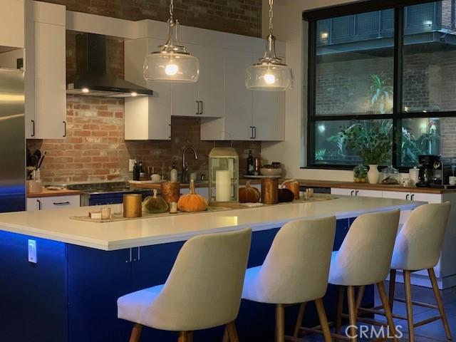 kitchen featuring white cabinetry, blue cabinetry, wall chimney exhaust hood, and a kitchen bar