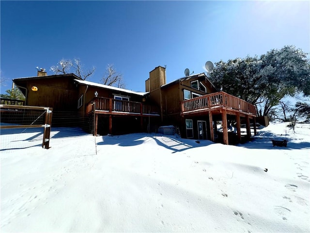 snow covered back of property with a chimney and a deck