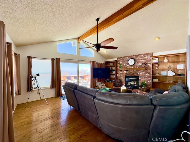 living room with a ceiling fan, lofted ceiling with beams, a textured ceiling, hardwood / wood-style floors, and a brick fireplace