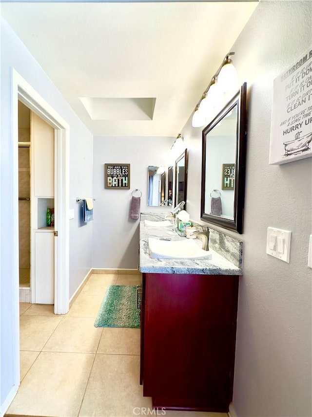 bathroom with baseboards, double vanity, a sink, a raised ceiling, and tile patterned floors