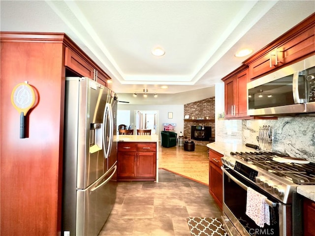 kitchen with decorative backsplash, appliances with stainless steel finishes, a raised ceiling, open floor plan, and reddish brown cabinets