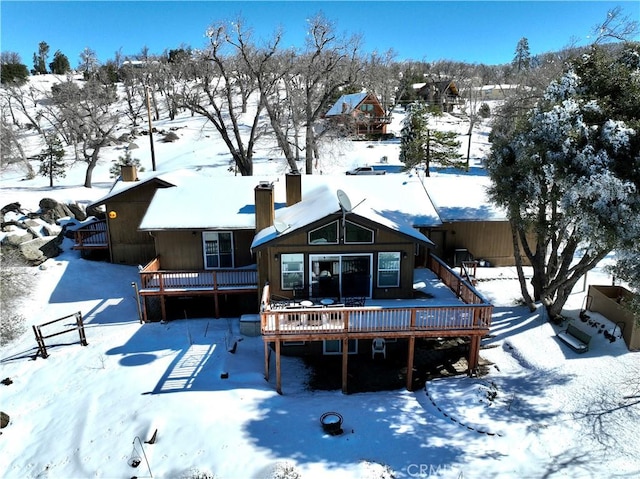 snow covered back of property featuring a deck and a chimney