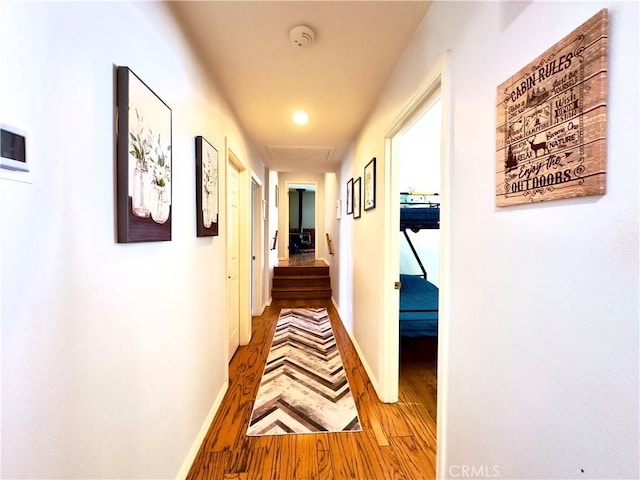 corridor featuring attic access, baseboards, and wood finished floors