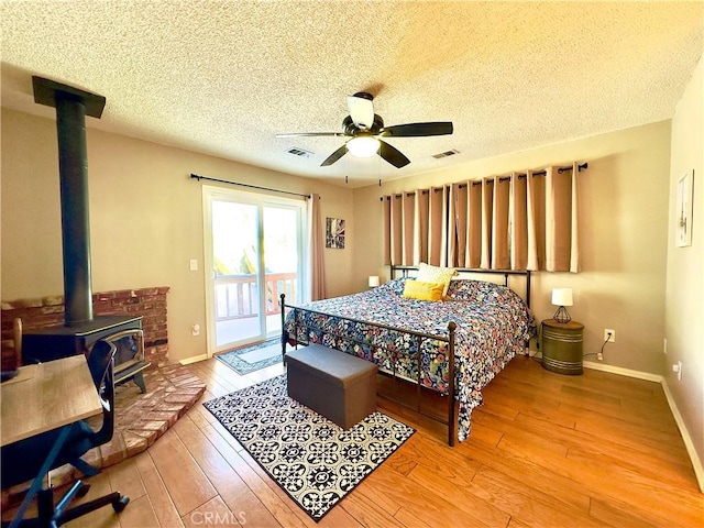 bedroom with baseboards, a wood stove, hardwood / wood-style flooring, a ceiling fan, and access to outside