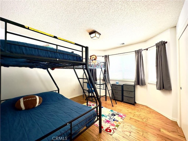 bedroom featuring visible vents, a textured ceiling, baseboards, and wood finished floors