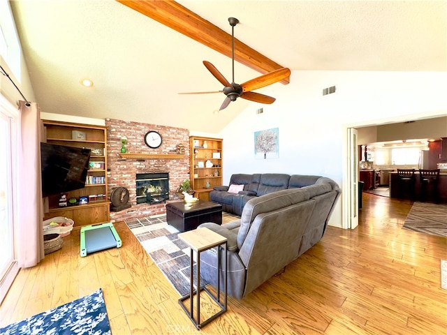 living area featuring beamed ceiling, visible vents, wood-type flooring, a textured ceiling, and a brick fireplace