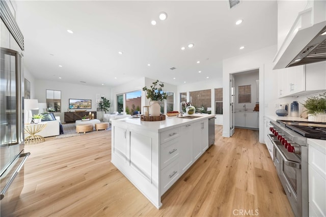 kitchen with white cabinetry, light wood finished floors, high quality appliances, and wall chimney range hood