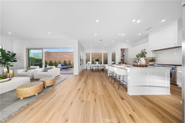 kitchen with open floor plan, high end stainless steel range, backsplash, light wood-style floors, and white cabinets