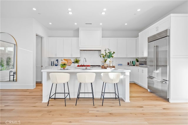 kitchen featuring built in refrigerator, light countertops, light wood-style floors, and a center island with sink