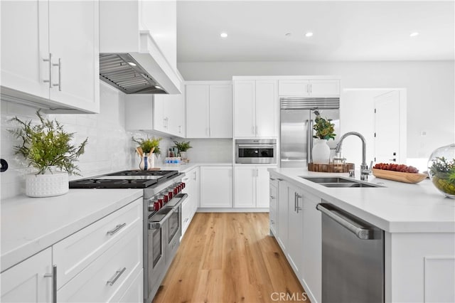 kitchen with a sink, white cabinetry, wall chimney exhaust hood, light countertops, and high end appliances