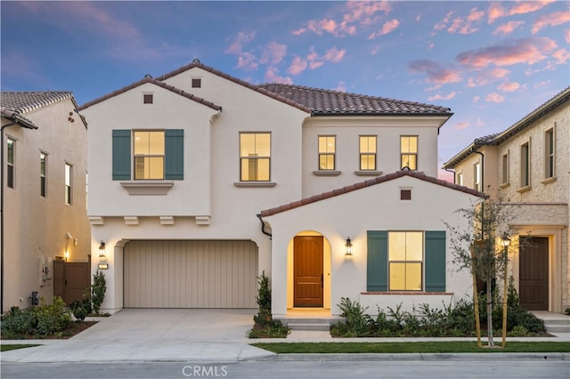 mediterranean / spanish-style home with stucco siding, a tiled roof, concrete driveway, and a garage