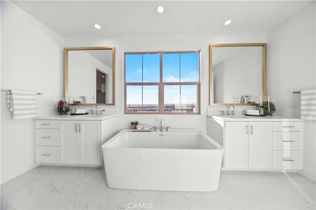 bathroom featuring marble finish floor, two vanities, a freestanding bath, and recessed lighting