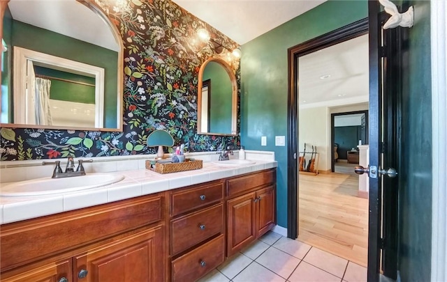 full bath featuring tile patterned flooring, double vanity, wallpapered walls, and a sink