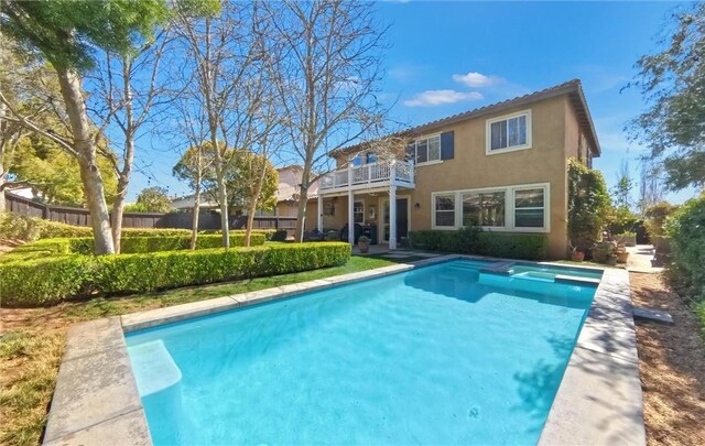 back of house featuring stucco siding, a balcony, a pool with connected hot tub, and fence