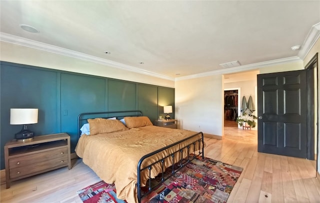 bedroom featuring visible vents, light wood-style flooring, ornamental molding, and a decorative wall