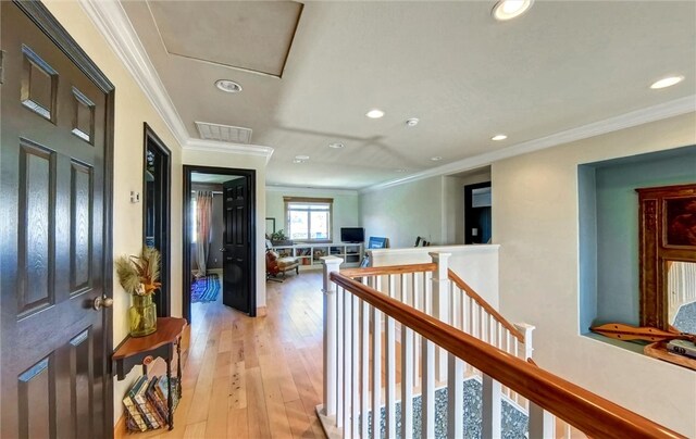 hallway with an upstairs landing, visible vents, light wood finished floors, and ornamental molding