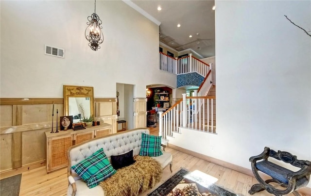 interior space featuring visible vents, light wood-style flooring, stairs, a towering ceiling, and a notable chandelier