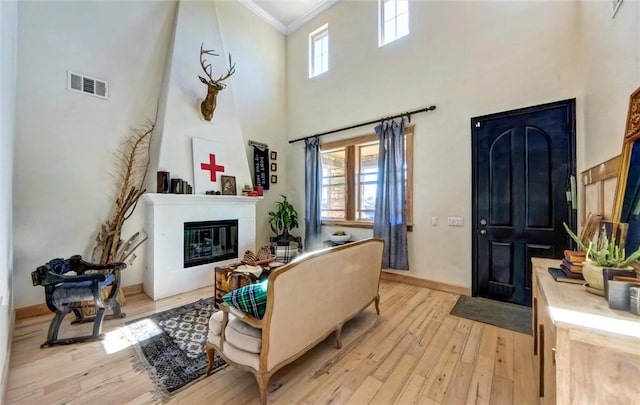 living area with baseboards, visible vents, a glass covered fireplace, crown molding, and light wood-type flooring