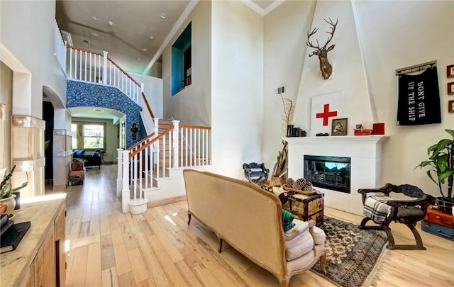 living area with stairs, a glass covered fireplace, arched walkways, and wood-type flooring