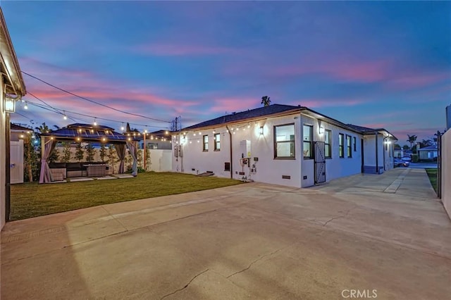 property exterior at dusk with stucco siding, a lawn, a patio, fence, and outdoor lounge area