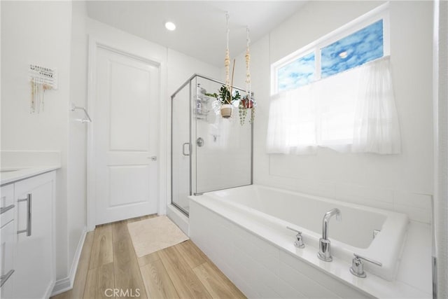 full bath featuring a bath, a stall shower, vanity, and wood finished floors