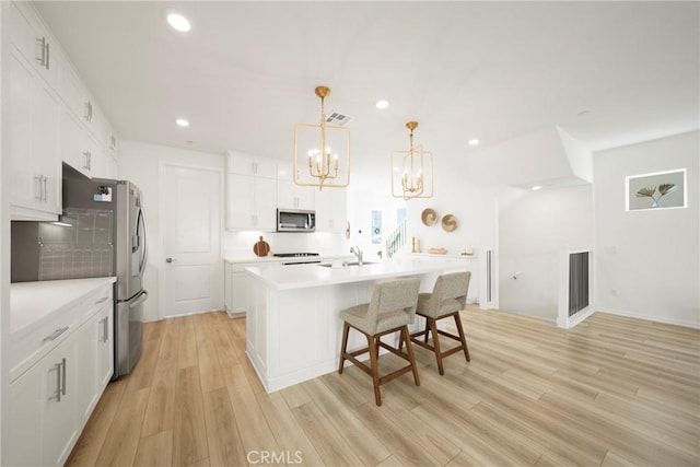 kitchen featuring visible vents, a kitchen island with sink, white cabinets, light wood-style floors, and appliances with stainless steel finishes