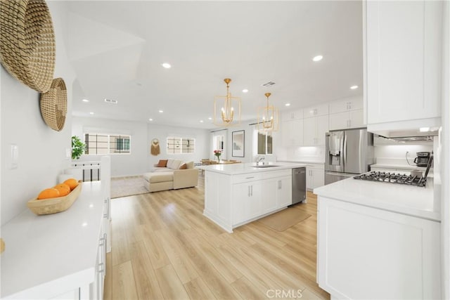 kitchen with a sink, a center island, stainless steel appliances, white cabinets, and light wood finished floors