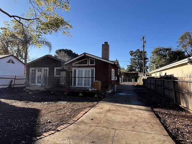 back of property with a deck, french doors, fence, and a chimney