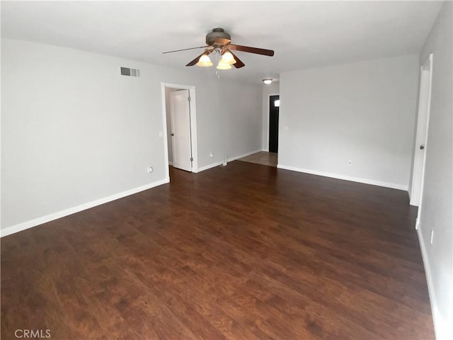 empty room featuring ceiling fan, visible vents, baseboards, and dark wood-style floors