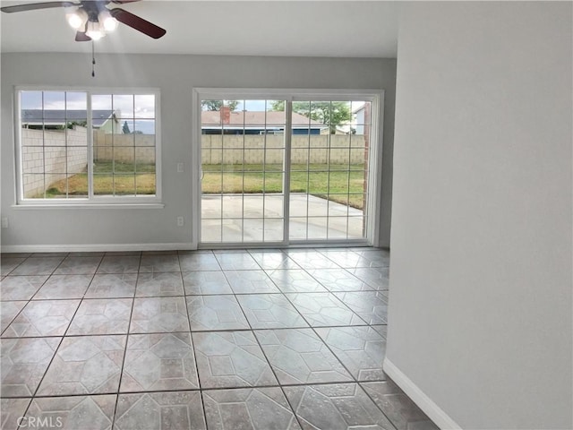 tiled empty room featuring ceiling fan and baseboards