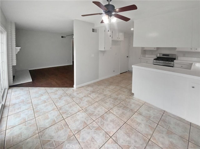 kitchen with gas stove, light tile patterned floors, light countertops, and white cabinetry