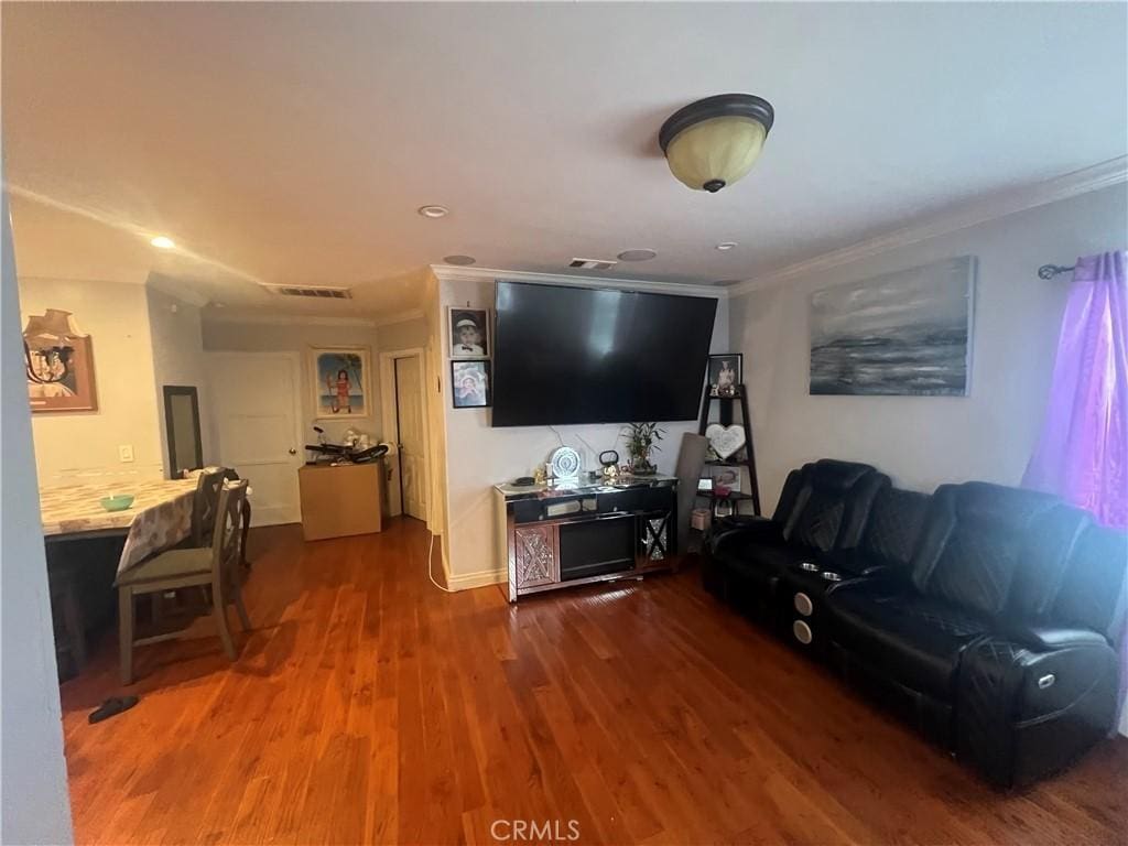 living room with crown molding, wood finished floors, and visible vents