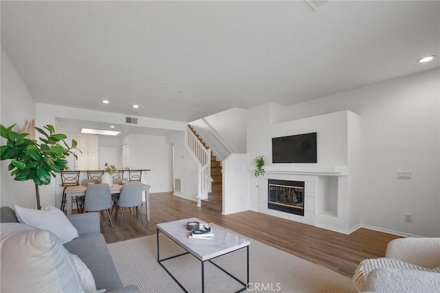 living room with wood finished floors, visible vents, recessed lighting, stairs, and a tiled fireplace