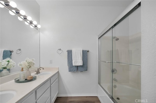 full bathroom featuring a sink, wood finished floors, combined bath / shower with glass door, double vanity, and baseboards