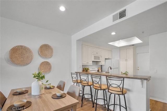 kitchen featuring visible vents, white appliances, a peninsula, a breakfast bar area, and a skylight