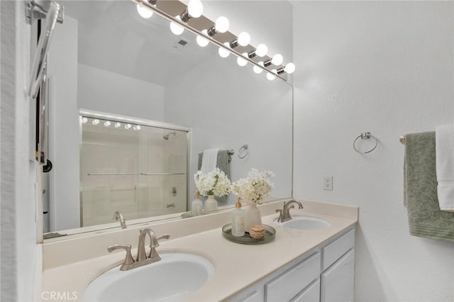 bathroom featuring double vanity, visible vents, a shower with door, and a sink